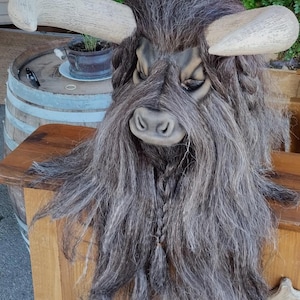 May include: A grey and brown furry mask with horns, resembling a mythical creature. The mask has a braided beard and a realistic face.