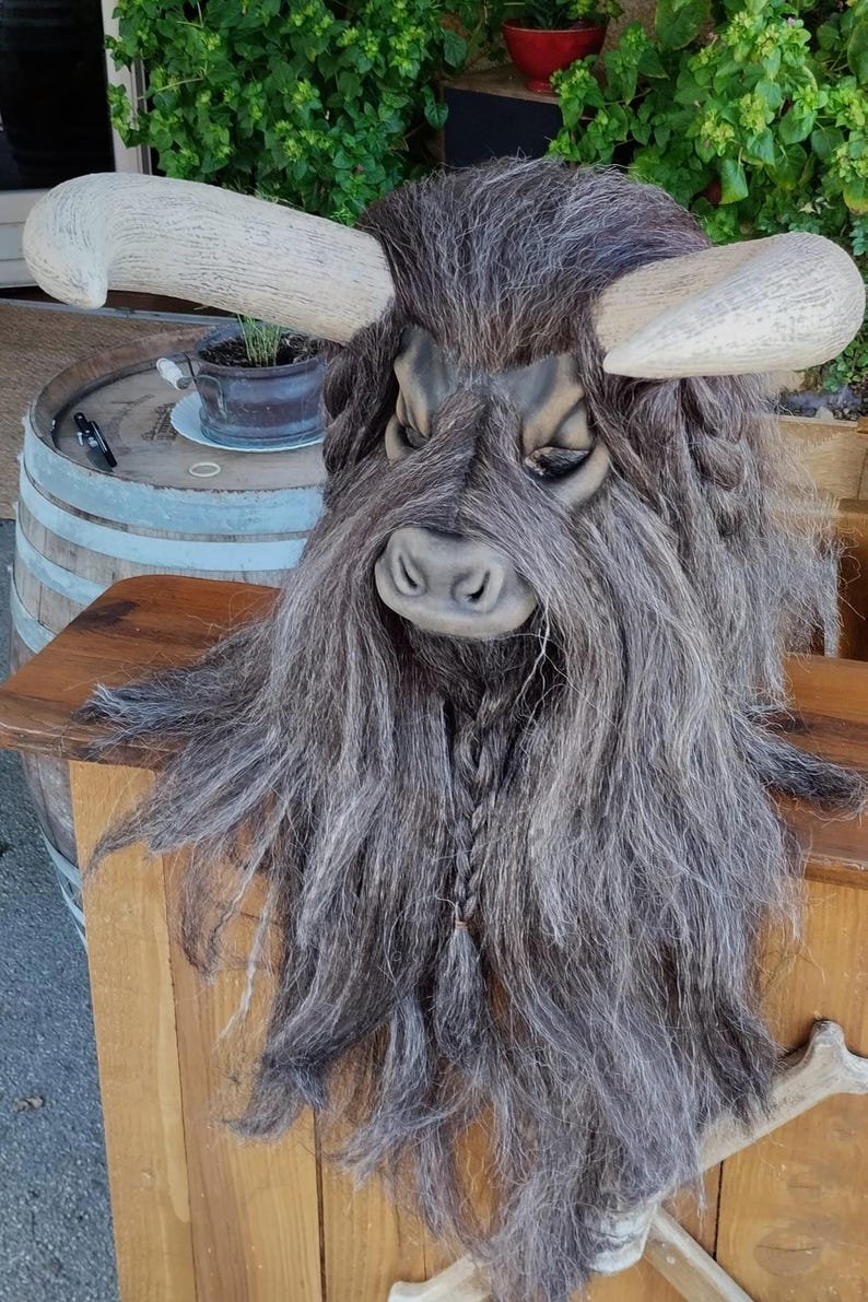 May include: A grey and brown furry mask with horns, resembling a mythical creature. The mask has a braided beard and a realistic face.