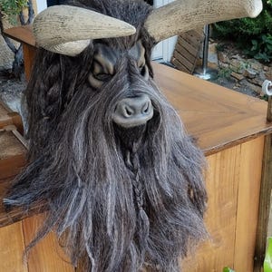 May include: A brown and black bull mask with long, grey hair and horns. The mask is made of a hard material and has a realistic look.