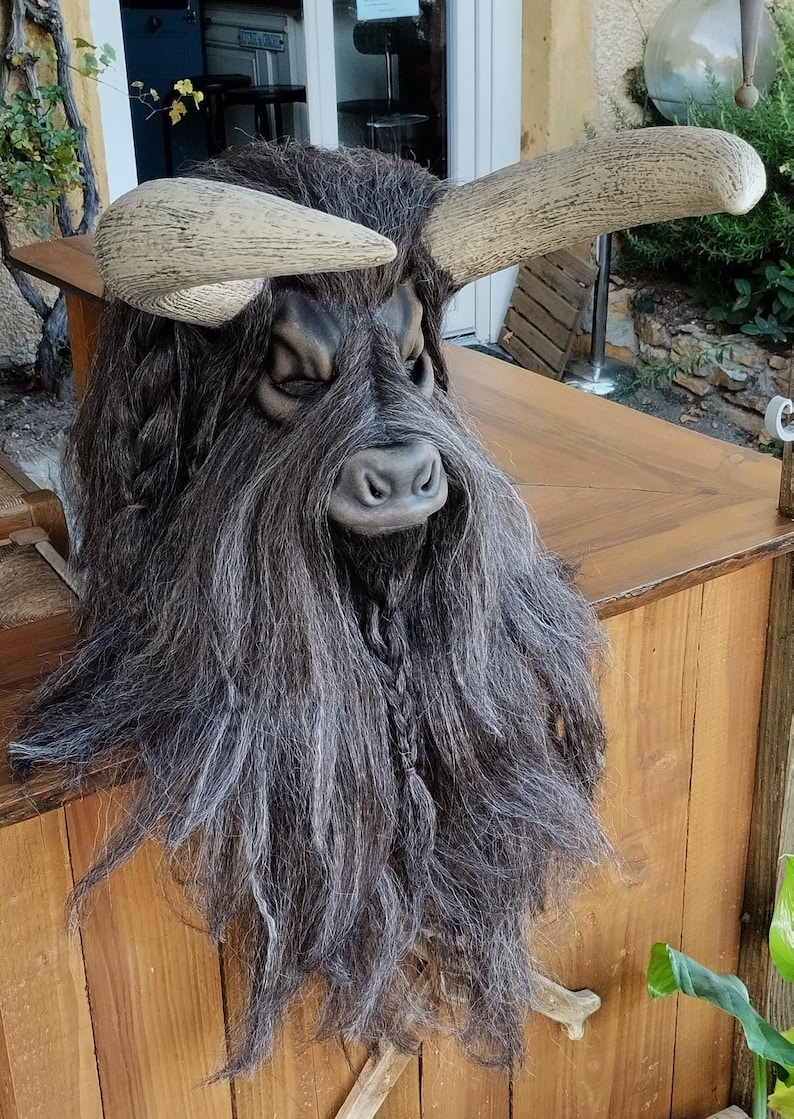May include: A brown and black bull mask with long, grey hair and horns. The mask is made of a hard material and has a realistic look.