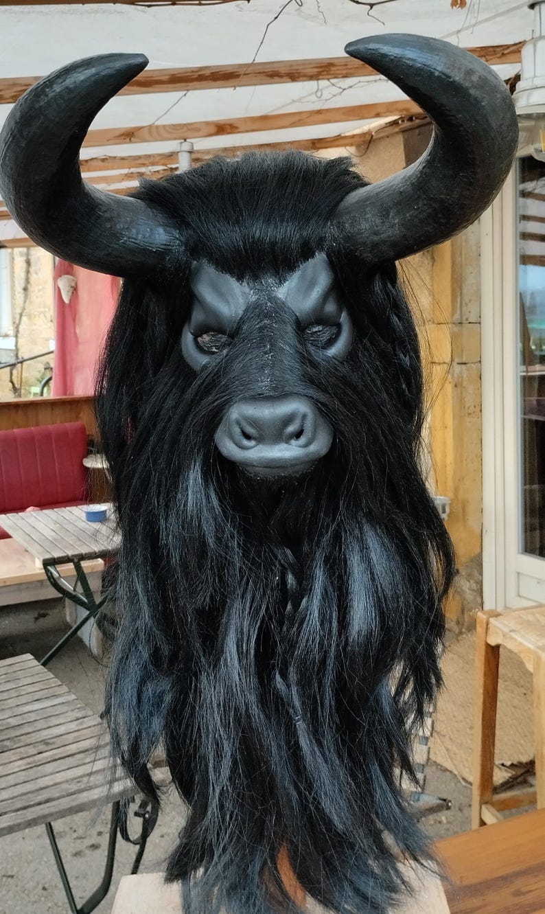 May include: A black bull mask with long, black hair and horns. The mask has a detailed face with a black nose and eyes.