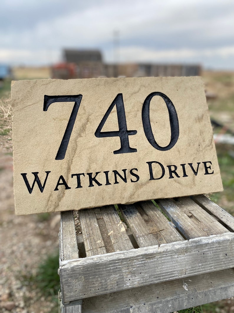 May include: A beige stone house number sign with black lettering. The number is 740 and the street name is Watkins Drive.