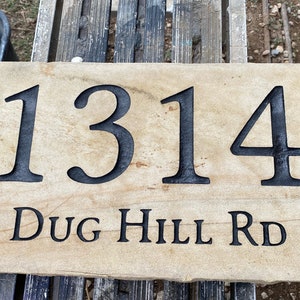 May include: A light brown stone house number sign with black lettering. The number 1314 is displayed in a large font, with the street name "DUG HILL RD" in a smaller font below.