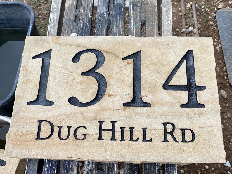 May include: A light brown stone house number sign with black lettering. The number 1314 is displayed in a large font, with the street name "DUG HILL RD" in a smaller font below.