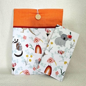 May include: A fabric pouch and a matching wallet featuring a white background with a pattern of koalas, birds, rainbows, and flowers. The pouch has an orange top section with a wooden button closure, while the wallet features a red button.