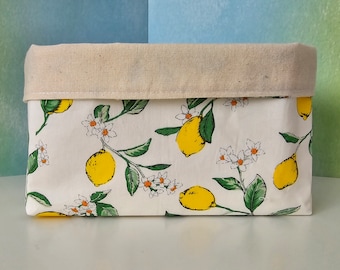 Op de afbeelding: Een witte stoffen opbergmand met een citroen- en bloemenprint. De mand heeft een beige canvas bovenkant en een witte basis met een citroen- en bloemenprint.