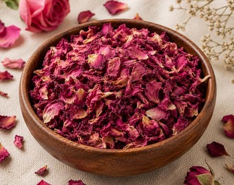 May include: A round wooden bowl filled with dried rose petals in shades of deep magenta, pink, and light cream. The petals have a textured, crinkled appearance. A single fresh pink rose and scattered loose petals surround the wooden bowl.