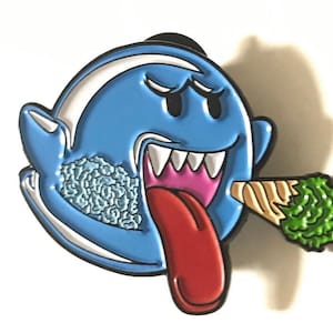 May include: Blue and white enamel pin of a cartoon ghost with a large, red tongue sticking out. The ghost is holding a green and brown marijuana joint in its mouth.