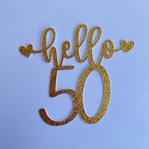 Pode incluir: Topo de bolo de glitter dourado com as palavras "hello 50" e dois pequenos corações.