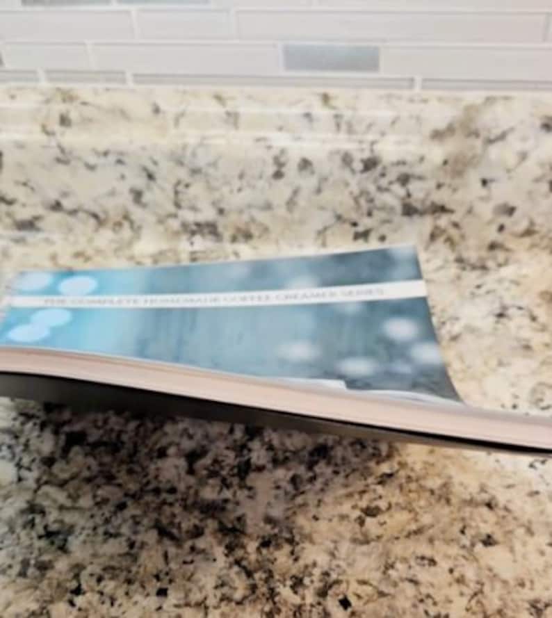 May include: A close-up of a book titled "The Complete From-Scratch Coffee Creamer Series". The book cover features a blue and white abstract design with a blurred background.
