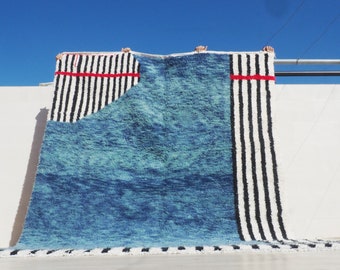 Puede incluir: Una alfombra de rayas azules y blancas con detalles rojos. La alfombra está hecha de lana y tiene una textura tejida a mano.