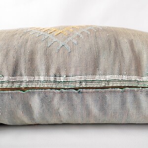 May include: A long, rectangular decorative pillow in shades of gray with embroidered geometric patterns in yellow, white, and blue. The pillow has a zipper closure and a textured fabric.