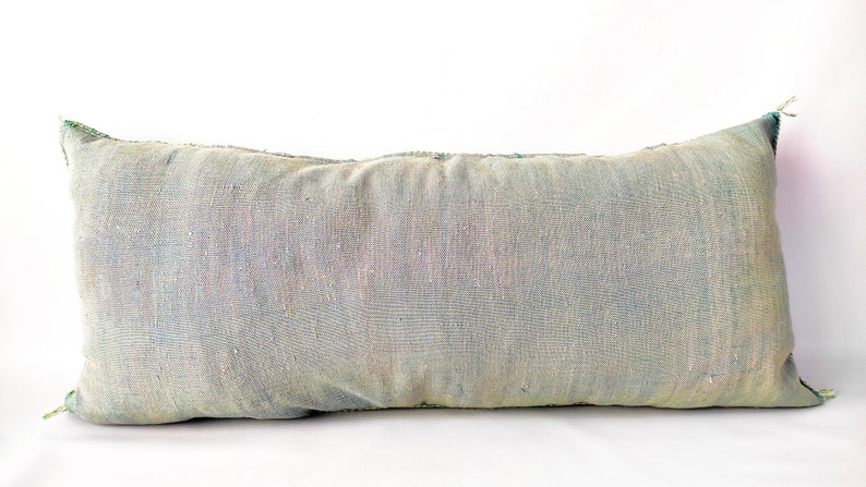 May include: A rectangular, light blue decorative pillow with a textured fabric. The pillow has a faded appearance with hints of green and blue. The edges are finished with green stitching. This pillow is perfect for adding a touch of color to any room.