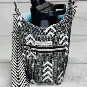 May include: Black and white patterned water bottle holder with a chevron strap. The holder has a zipper pocket and a light blue interior. A black water bottle is inside the holder. The text "Payneless Creations" is visible.