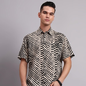 May include: Short-sleeved shirt featuring a black and cream zebra stripe design. The shirt has a collared neckline and a single chest pocket. The fabric is lightweight.