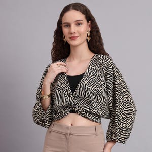 Peut inclure: Un haut court à imprimé zébré noir et blanc avec des manches longues. Le haut est noué à la taille et porté avec un pantalon beige. Le modèle porte des bijoux dorés.