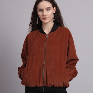 Peut inclure: Veste de bombardier en velours côtelé de couleur rouille avec col et poignets noirs. La veste a une fermeture éclair sur toute la longueur et deux poches avant. Le modèle porte un pantalon noir.