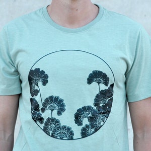 May include: A light green t-shirt with a circular design featuring black stylized flowers.