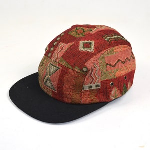 Op de afbeelding: Een 5-paneels pet met een rood, groen en beige patroon en een zwarte klep.
