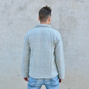 Puede incluir: Una camisa de manga larga de color gris claro con cuello abotonado. La camisa est&aacute; hecha de una tela suave y texturizada.