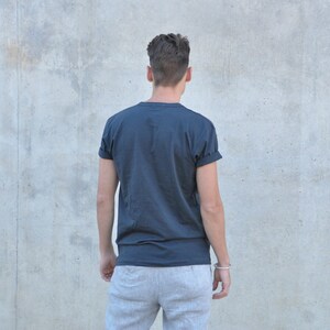 Pu&ograve; includere: Una persona indossa una maglietta blu scuro con le maniche arrotolate e pantaloni della tuta grigi.