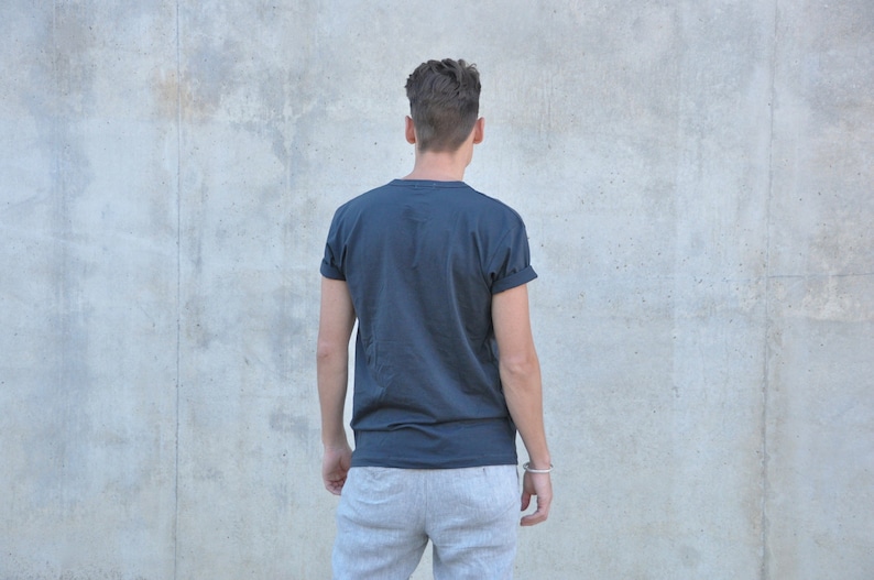 Pu&ograve; includere: Una persona indossa una maglietta blu scuro con le maniche arrotolate e pantaloni della tuta grigi.