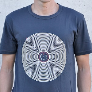 Pu&ograve; includere: Una t-shirt blu scuro con una grafica bianca di un disco con cerchi concentrici e il testo "Lost in Music" al centro.