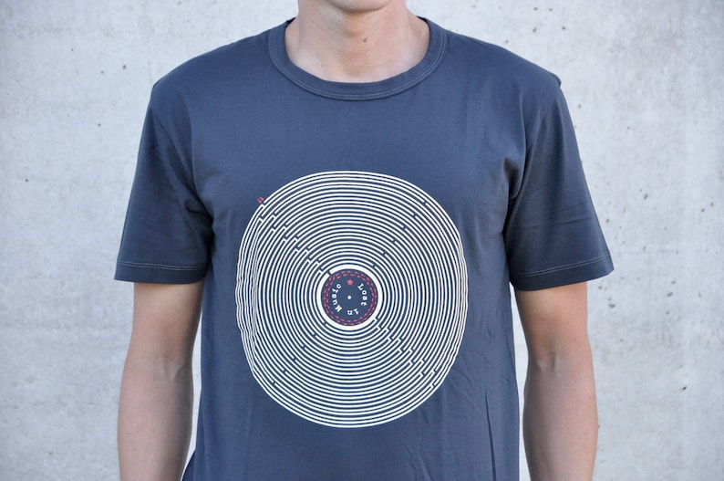 Pu&ograve; includere: Una t-shirt blu scuro con una grafica bianca di un disco con cerchi concentrici e il testo "Lost in Music" al centro.