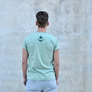 May include: A light green t-shirt with a black and white graphic of a crescent moon and a lotus flower on the back.