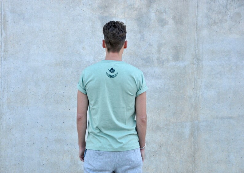May include: A light green t-shirt with a black and white graphic of a crescent moon and a lotus flower on the back.