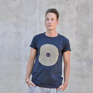 Pu&ograve; includere: Una t-shirt blu scuro con un design circolare in beige e marrone. Il design presenta cerchi concentrici e un cerchio pi&ugrave; piccolo al centro con un motivo a stella.