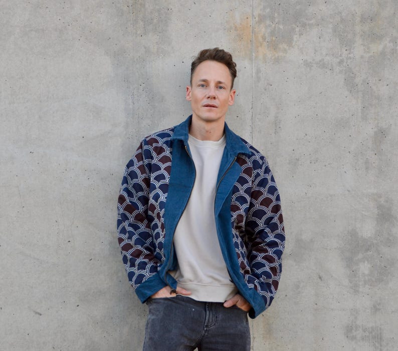 Peut inclure: Un homme portant une veste en jean bleue avec une doublure &agrave; motifs blancs et bleus. La veste a une fermeture &eacute;clair et un col. L'homme porte un t-shirt blanc sous la veste et un jean bleu.