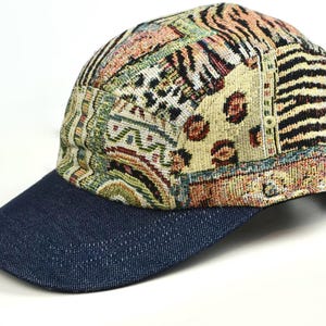 May include: A baseball cap with a denim blue brim and a patterned crown. The crown features a patchwork design with various patterns, including animal prints and geometric shapes, in shades of beige, brown, and black.