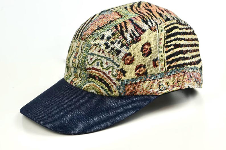 May include: A baseball cap with a denim blue brim and a patterned crown. The crown features a patchwork design with various patterns, including animal prints and geometric shapes, in shades of beige, brown, and black.