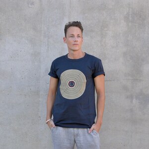 Pu&ograve; includere: Una t-shirt blu navy con un design circolare in oro e marrone. Il design presenta cerchi concentrici con un cerchio pi&ugrave; piccolo al centro.