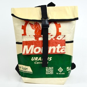 Peut inclure: Sac à dos crème avec des détails noirs et une fermeture à boucle noire. Le devant présente un logo rouge et blanc avec le mot "Mounta" et du texte vert qui dit "URAN IS Cement". Le sac a des sangles noires.