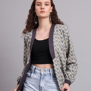 Pode incluir: Casaco bege e azul estampado com acabamento roxo escuro. O casaco tem um design de decote em V e mangas compridas. A modelo usa um top preto e jeans azul claro.