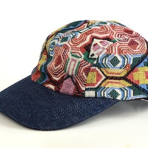 Op de afbeelding: Een baseballpet met een denimblauwe klep en een kleurrijke patroon kroon. De kroon heeft een geometrisch ontwerp met rode, gele, groene en roze tinten. De pet staat tegen een witte achtergrond.