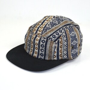 Puede incluir: Una gorra de 5 paneles con estampado en blanco y negro y visera negra. La gorra tiene un patrón geométrico con detalles marrones.