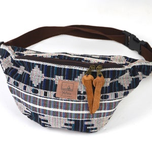 Può includere: Una marsupio con motivo bianco e blu, con una tracolla marrone e una chiusura a zip. La marsupio ha un'etichetta in pelle marrone con la parola "Yatra" su di essa.