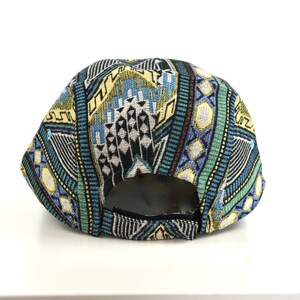 May include: A colorful baseball cap with a geometric pattern in shades of blue, green, yellow, and black. The cap has a curved brim and an adjustable strap at the back. The cap is made of a woven fabric.