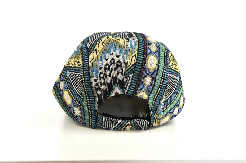May include: A colorful baseball cap with a geometric pattern in shades of blue, green, yellow, and black. The cap has a curved brim and an adjustable strap at the back. The cap is made of a woven fabric.
