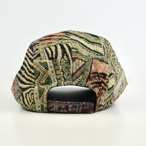 May include: A patterned baseball cap with a tapestry design. The cap features a mix of colors including beige, green, and brown. The back of the cap has an adjustable strap. The cap is made of a woven fabric.