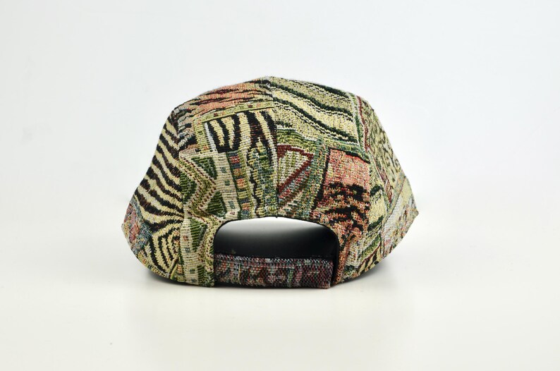 May include: A patterned baseball cap with a tapestry design. The cap features a mix of colors including beige, green, and brown. The back of the cap has an adjustable strap. The cap is made of a woven fabric.