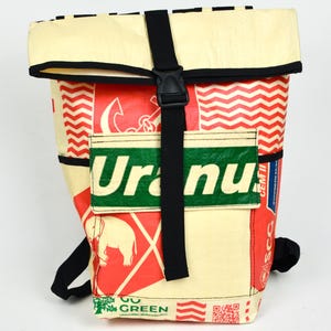 Könnte beinhalten: Ein Rolltop-Rucksack aus recyceltem Material in den Farben Creme, Rot und Grün. Auf der Vorderseite befindet sich ein grüner rechteckiger Aufnäher mit dem Text "Uranus" und einem Elefanten-Motiv. Ein schwarzer Riemen mit Schnalle sichert das Oberteil.