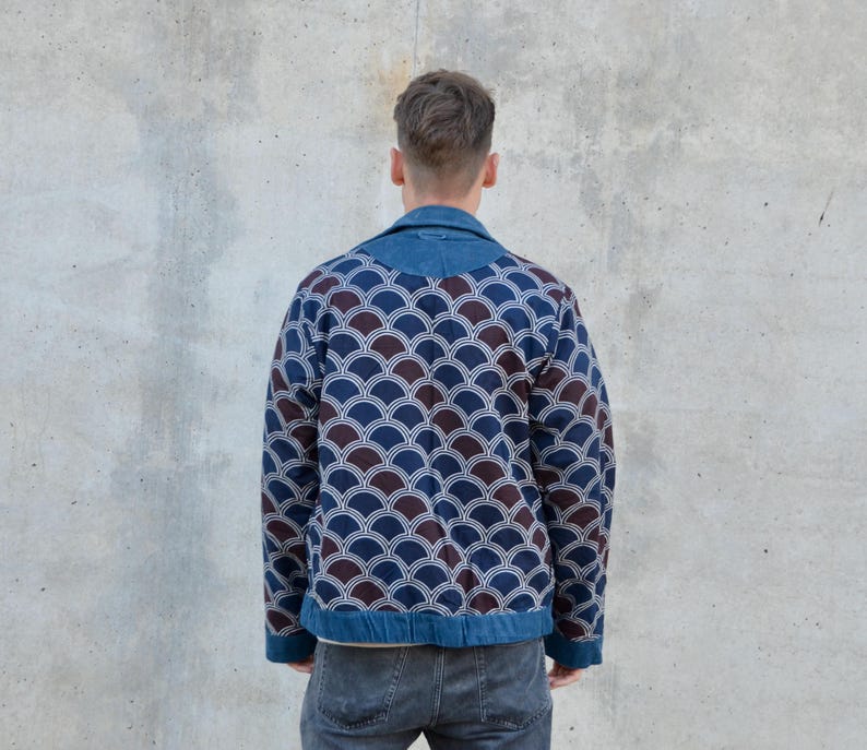 Peut inclure: Une veste en jean bleue avec un motif g&eacute;om&eacute;trique brun et bleu. La veste a un col et une fermeture &eacute;clair.
