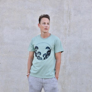 May include: A light green t-shirt with a circular graphic of dark green trees in a circle.