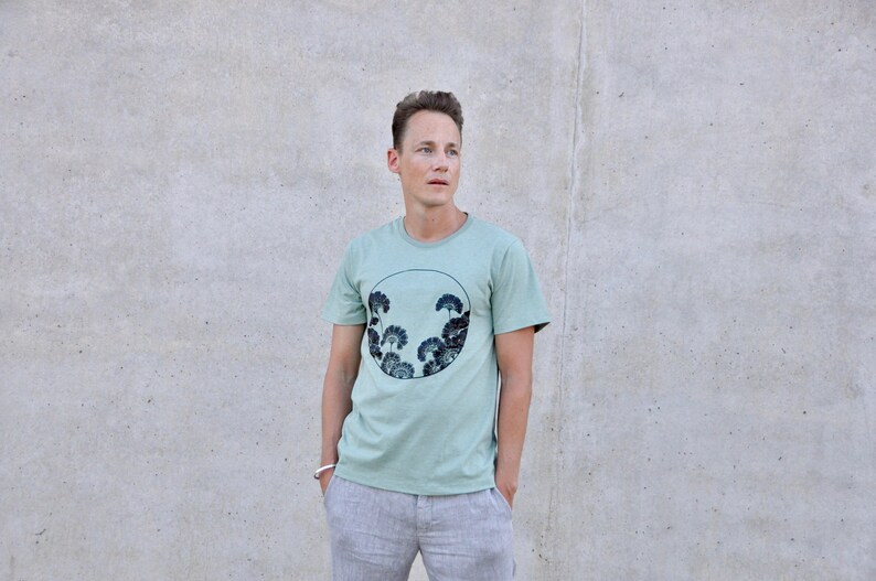 May include: A light green t-shirt with a circular graphic of dark green trees in a circle.
