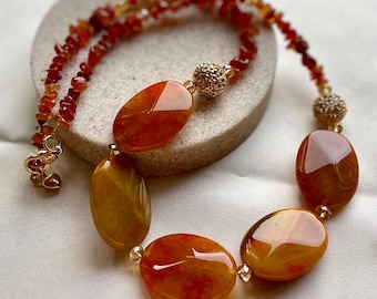 May include: A long necklace made with orange and yellow agate stones and gold accents. The necklace features large oval-shaped stones and smaller, round stones.