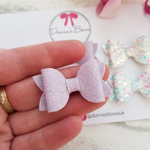 Peut inclure: Un n&oelig;ud en paillettes de couleur violet clair avec un centre blanc. Le n&oelig;ud est fait &agrave; la main et est parfait pour ajouter une touche d'&eacute;clat &agrave; n'importe quelle tenue.